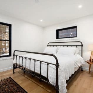 A bright finished bedroom with an iron bed, white-oak floors, and black-trimmed windows. Home addition project by Potts Brothers Construction, Arlington & Northern Virginia