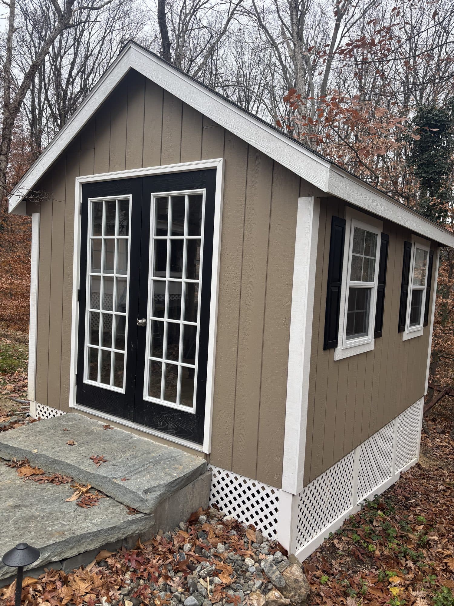 A completed detached studio with board-and-batten siding, black-shuttered windows, and French doors over a stone step. Home addition project by Potts Brothers Construction, Arlington & Northern Virginia