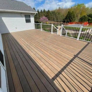 A newly built composite deck with two-tone decking, white posts, and black aluminum railing off a sided home. Home addition project by Potts Brothers Construction, Arlington & Northern Virginia