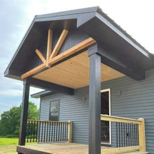 A covered porch addition with a timber sunburst gable bracket, dark posts, and a new wood deck on a gray-sided home. Home addition project by Potts Brothers Construction, Arlington & Northern Virginia