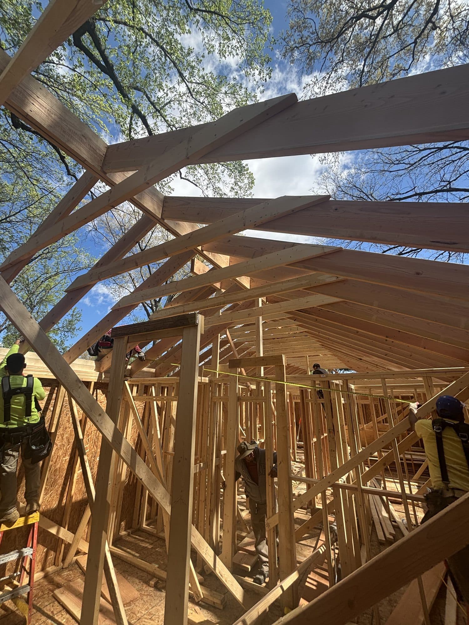 An upward view of a crew framing rafters and wall studs over a new addition against blue sky. Home addition project by Potts Brothers Construction, Arlington & Northern Virginia