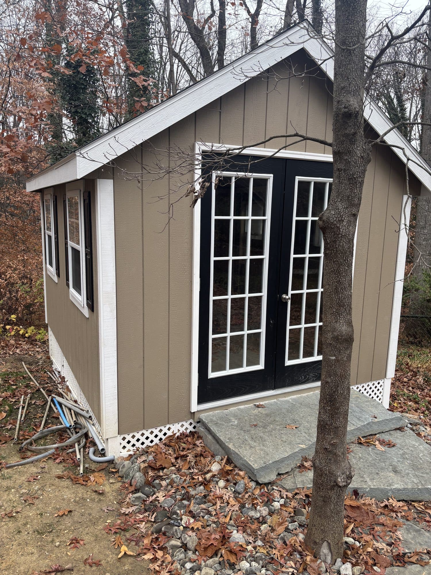 A detached garden studio with board-and-batten siding and double French doors over a stone landing. Home addition project by Potts Brothers Construction, Arlington & Northern Virginia
