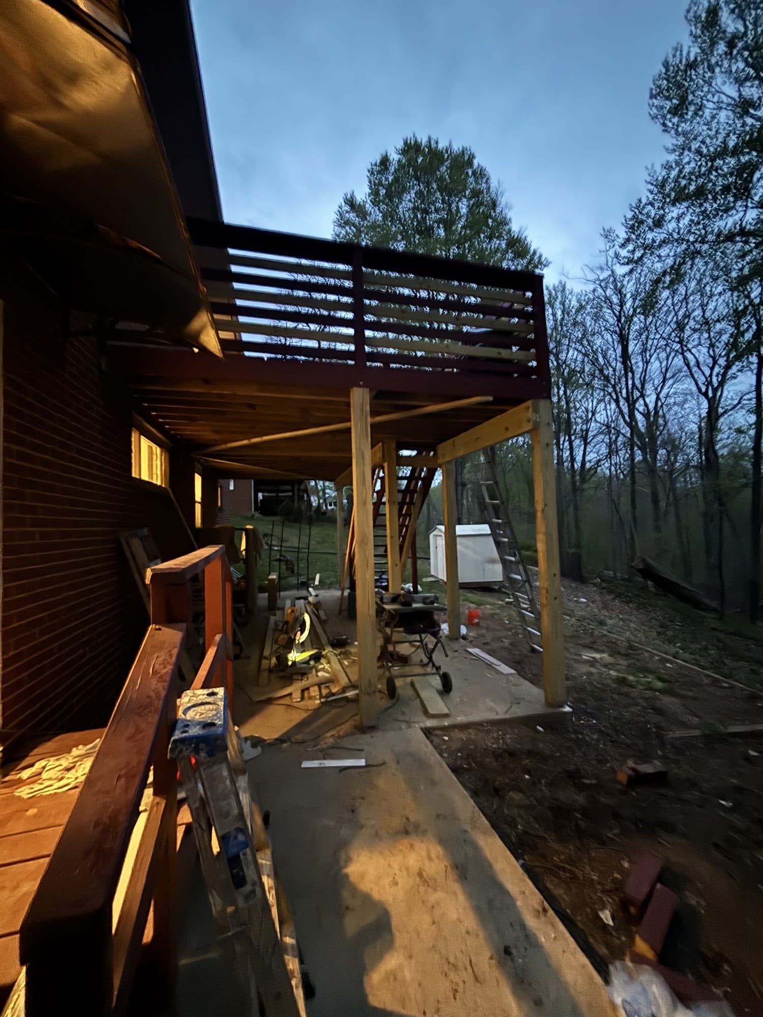An elevated rear deck framed on posts above a patio, with stairs descending to the yard at dusk. Home addition project by Potts Brothers Construction, Arlington & Northern Virginia