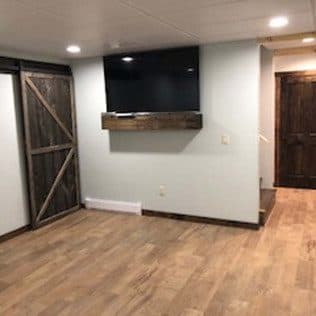 A finished basement with a sliding barn door, a mounted TV on a floating mantel, and wood-look flooring. Home addition project by Potts Brothers Construction, Arlington & Northern Virginia