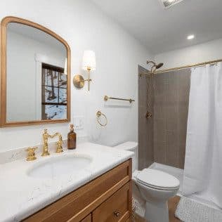 A finished bathroom with a marble-top wood vanity, brass fixtures, and a tiled tub-shower surround. Home addition project by Potts Brothers Construction, Arlington & Northern Virginia