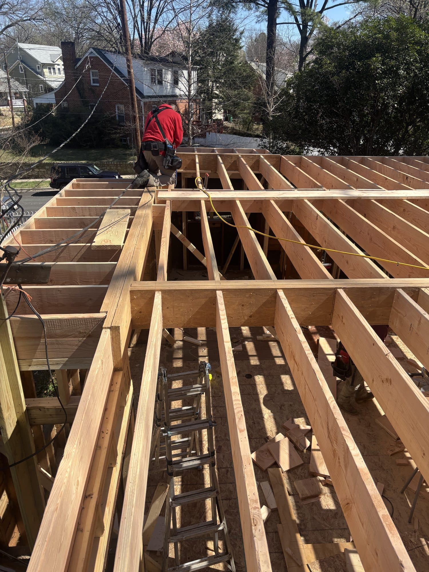 A worker drills into freshly framed floor joists of a second-story addition with a brick home behind. Home addition project by Potts Brothers Construction, Arlington & Northern Virginia