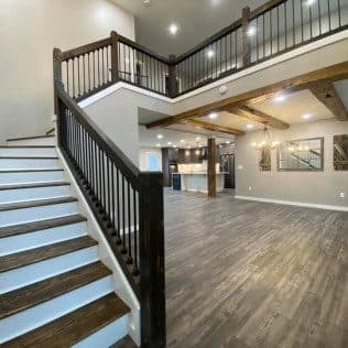 A finished open-concept great room with a dark-stained staircase, exposed beams, and wide-plank flooring. Home addition project by Potts Brothers Construction, Arlington & Northern Virginia