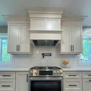 A remodeled kitchen with a custom paneled range hood, white cabinets, and a subway tile backsplash above a slide-in range. Home addition project by Potts Brothers Construction, Arlington & Northern Virginia