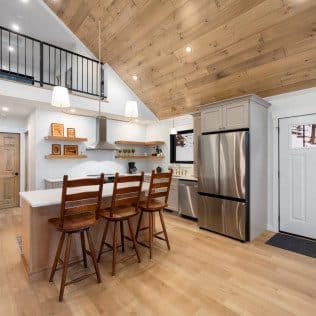 An open remodeled kitchen with a wood-plank vaulted ceiling, gray cabinets, and an island with wood bar stools. Home addition project by Potts Brothers Construction, Arlington & Northern Virginia