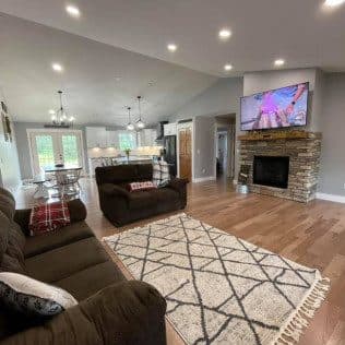 Living room with stone fireplace and open kitchen beyond. Home addition project by Potts Brothers Construction, Arlington & Northern Virginia