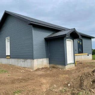 The exterior of a new addition with dark gray lap siding, a metal-clad gable, and a side entry door. Home addition project by Potts Brothers Construction, Arlington & Northern Virginia