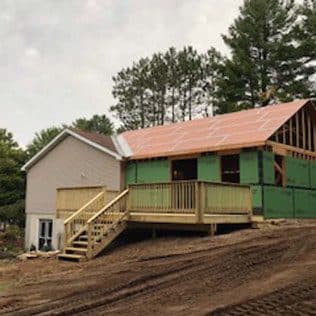 A ranch-home addition under construction with green sheathing, a new copper-toned metal gable, and a fresh wood deck. Home addition project by Potts Brothers Construction, Arlington & Northern Virginia