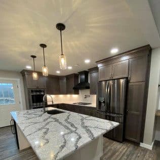 A remodeled kitchen with dark wood cabinets, a large veined-granite island, pendant lights, and stainless appliances. Home addition project by Potts Brothers Construction, Arlington & Northern Virginia