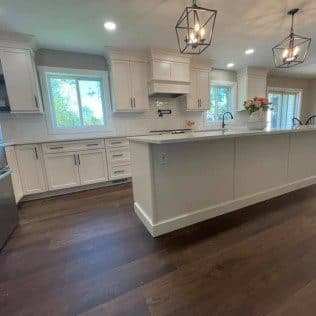 A remodeled kitchen with white shaker cabinets, a large center island, lantern pendants, and rich hardwood flooring. Home addition project by Potts Brothers Construction, Arlington & Northern Virginia