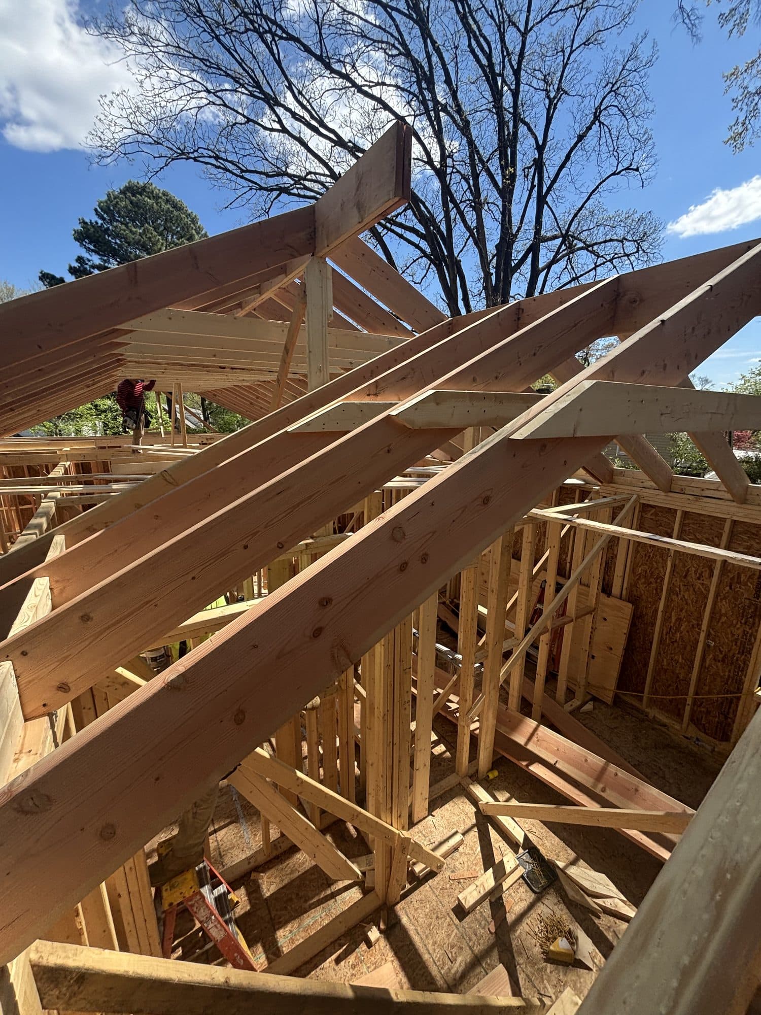 A worker frames large rafters over an addition under a bright blue sky. Home addition project by Potts Brothers Construction, Arlington & Northern Virginia