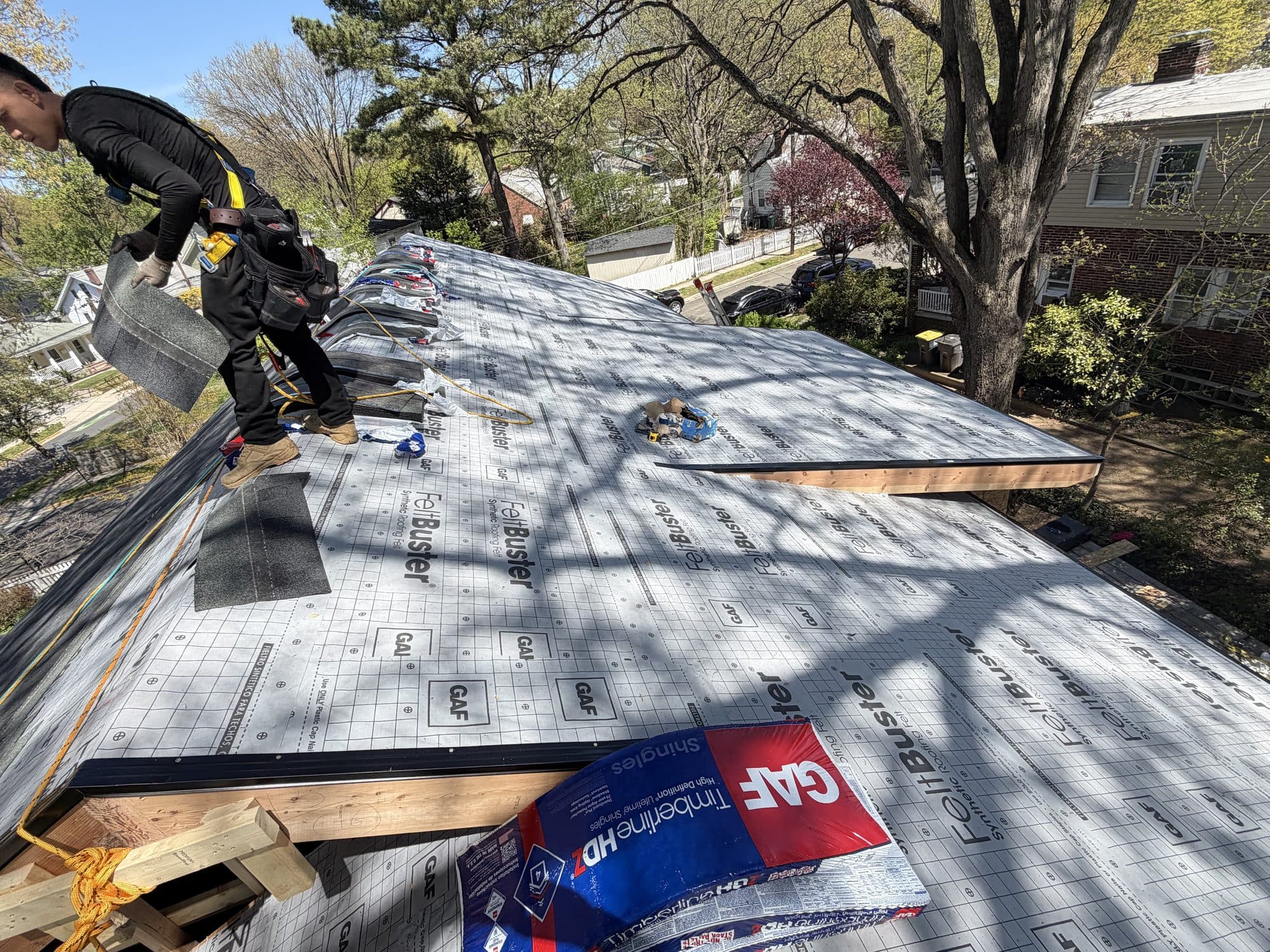 A worker installs synthetic underlayment across a wide sheathed deck during a re-shingle. Home addition project by Potts Brothers Construction, Arlington & Northern Virginia