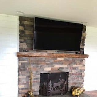 A finished stacked-stone fireplace with a reclaimed-wood mantel and wall-mounted television. Home addition project by Potts Brothers Construction, Arlington & Northern Virginia