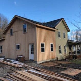 A two-story board-and-batten addition with new vertical wood siding joins an existing yellow farmhouse. Home addition project by Potts Brothers Construction, Arlington & Northern Virginia
