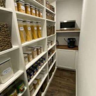 A finished walk-in pantry with custom white shelving, stocked containers, and a butcher-block counter. Home addition project by Potts Brothers Construction, Arlington & Northern Virginia