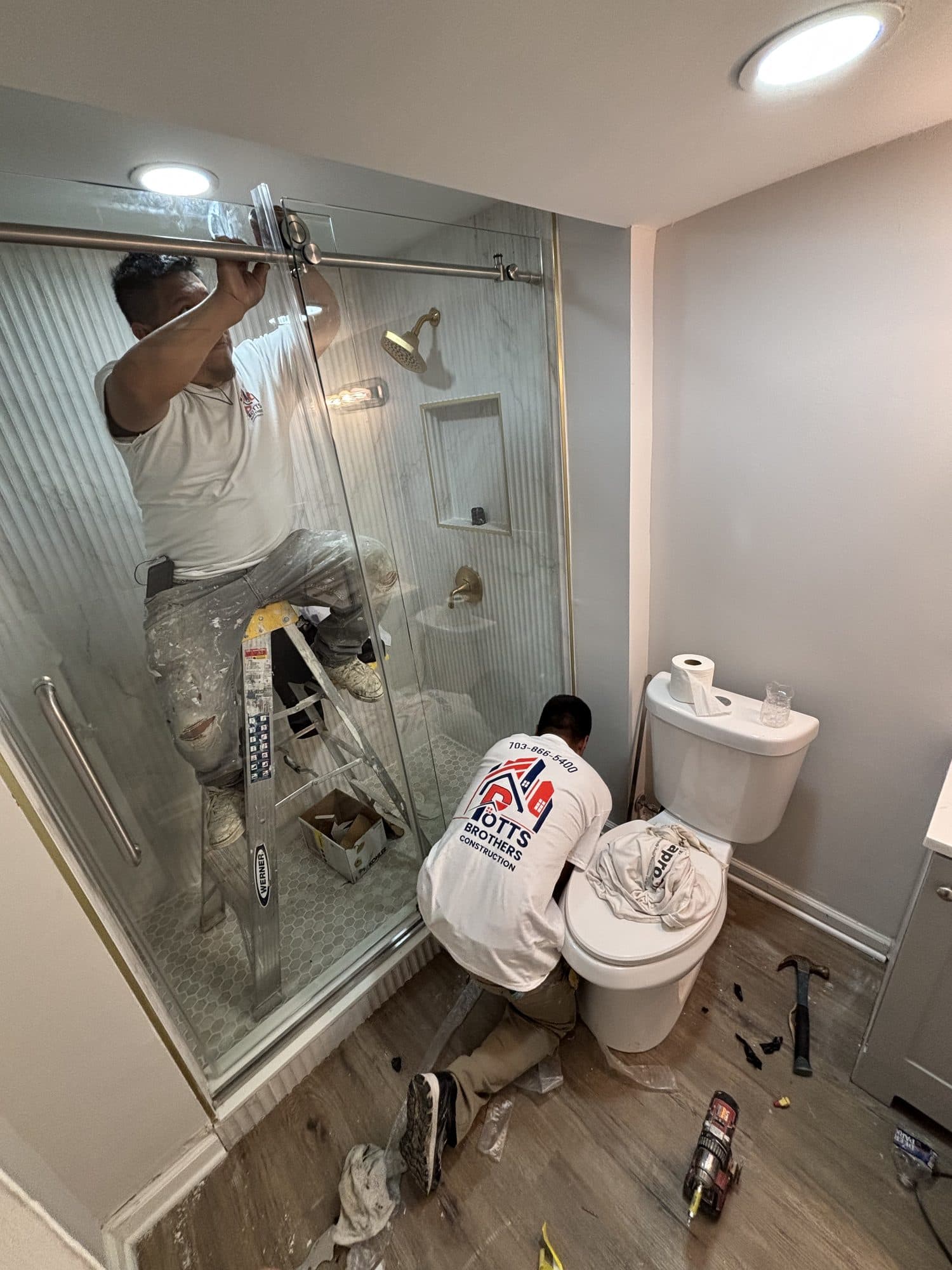 Worker installing glass shower door in remodeled. Home addition project by Potts Brothers Construction, Arlington & Northern Virginia