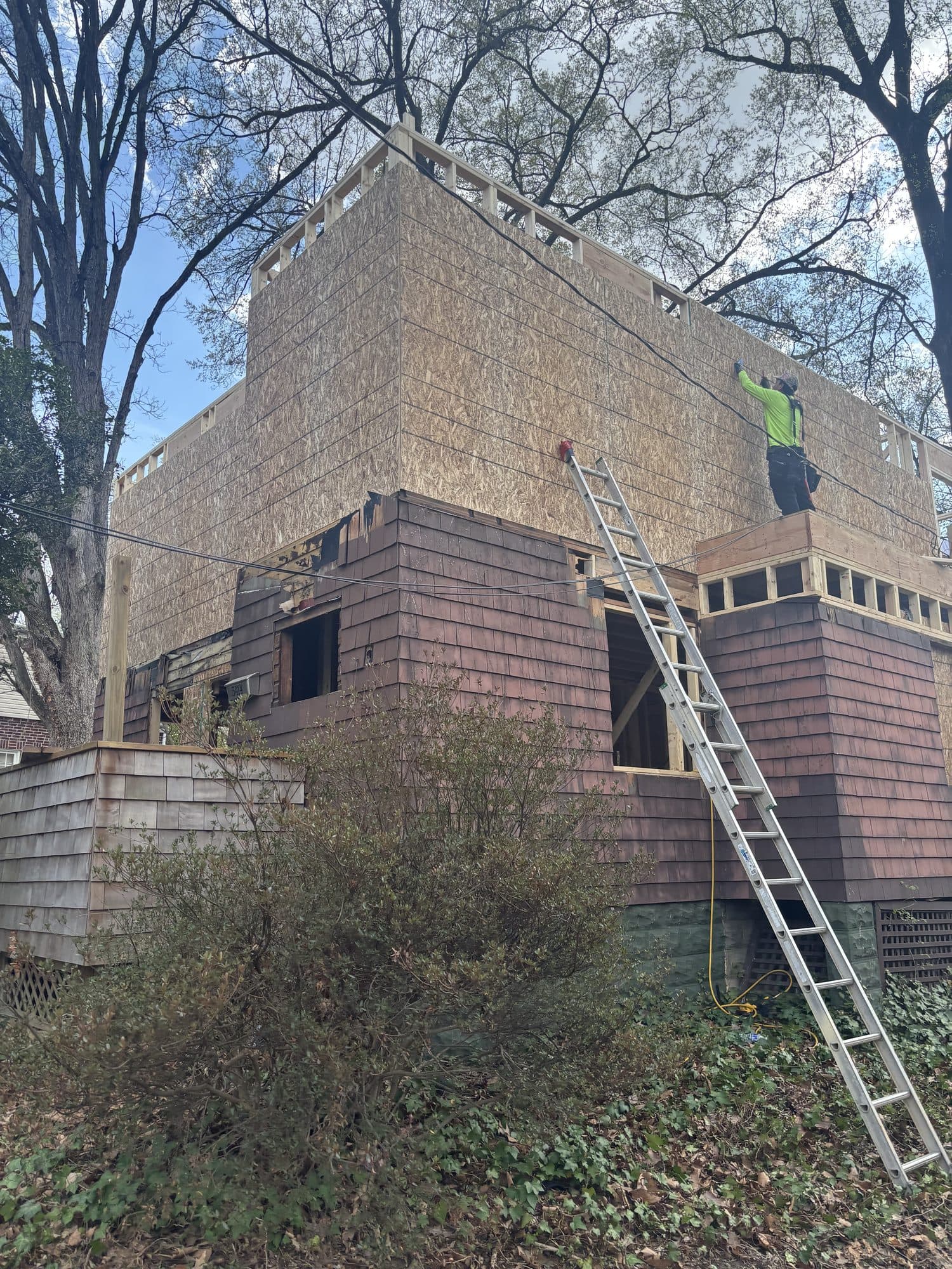 A worker sheathes a new second-story addition rising above the cedar-shake first floor of an existing home. Home addition project by Potts Brothers Construction, Arlington & Northern Virginia