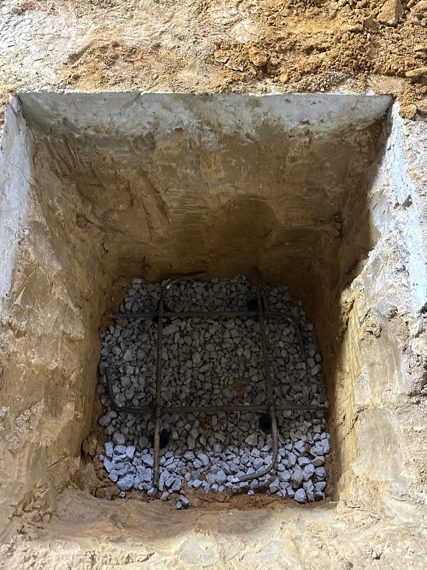 An excavated foundation footing pit lined with rebar cage set over crushed gravel within earthen walls. Foundation project by Potts Brothers Construction, Arlington & Northern Virginia