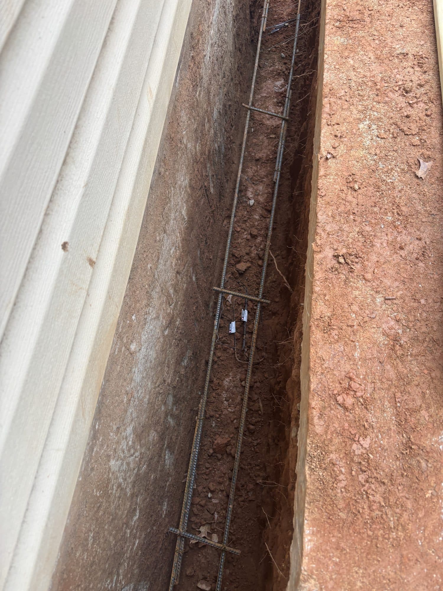 Long excavated foundation footing trench with continuous rebar reinforcement running alongside the structure. Foundation project by Potts Brothers Construction, Arlington & Northern Virginia